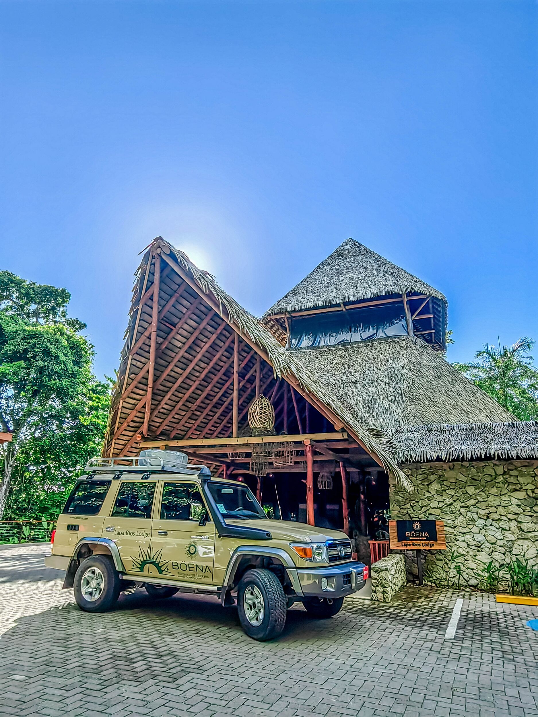 A safari vehicle parked in front of a lodge with a thatched roof and stone walls.