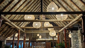A spacious indoor area with a high, thatched roof and hanging wicker chandeliers. There are stone pillars and wooden benches. - Lapa Rios Lodge (Puerto Jiménez)