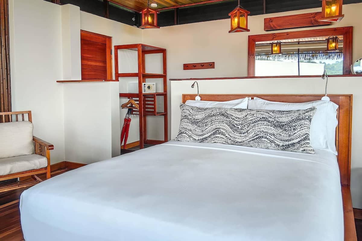 A bedroom with a wooden headboard, a bed with patterned pillows, a wooden wardrobe, and a hanging lantern.