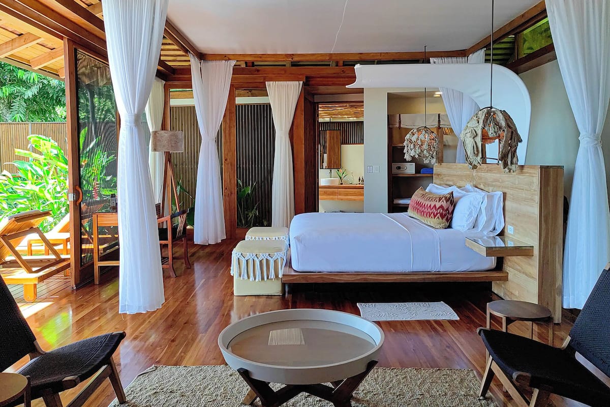 A bedroom with a bed, a bedside table, a chair, and a small table.