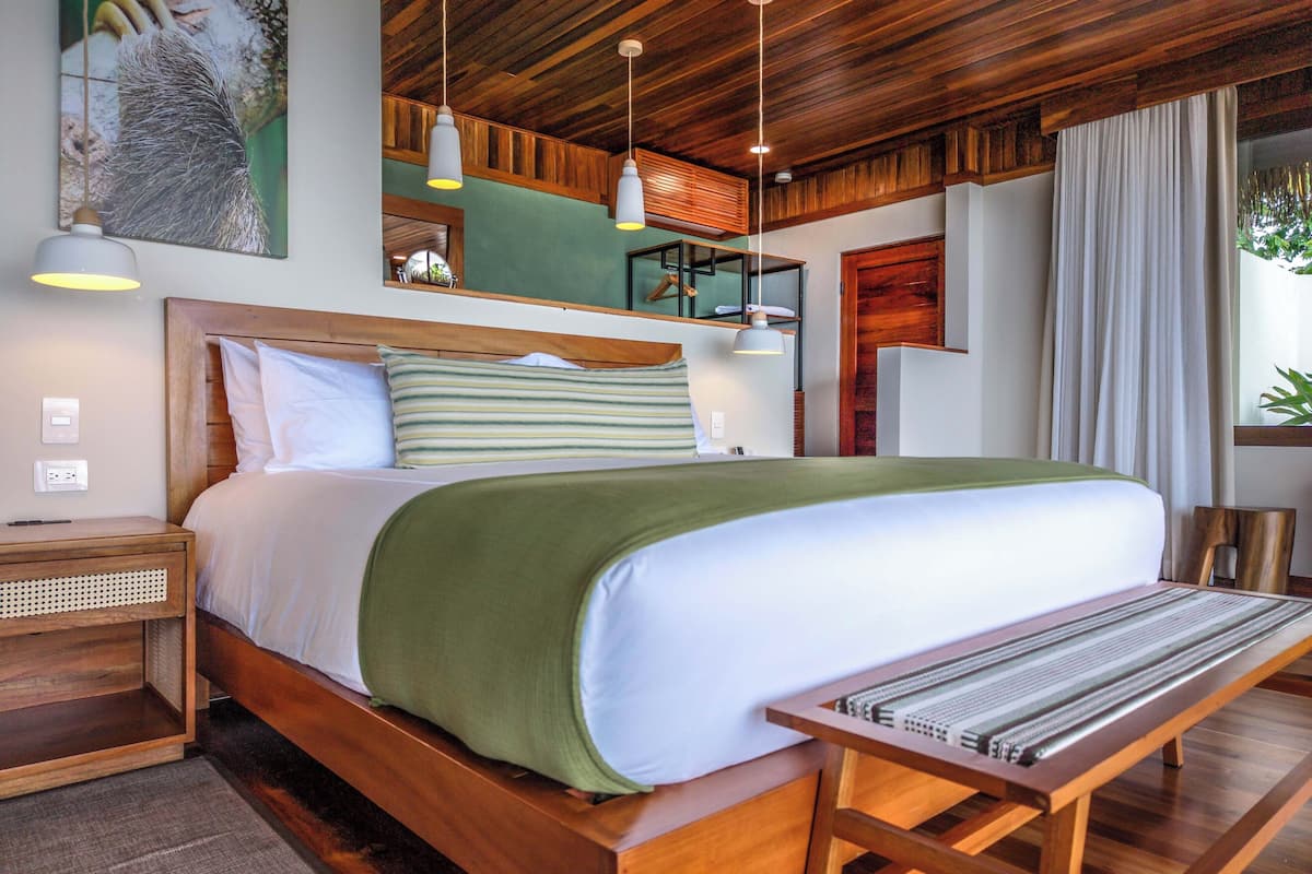 A neatly arranged bedroom with a large bed, bedside tables, a bench, and hanging lights.