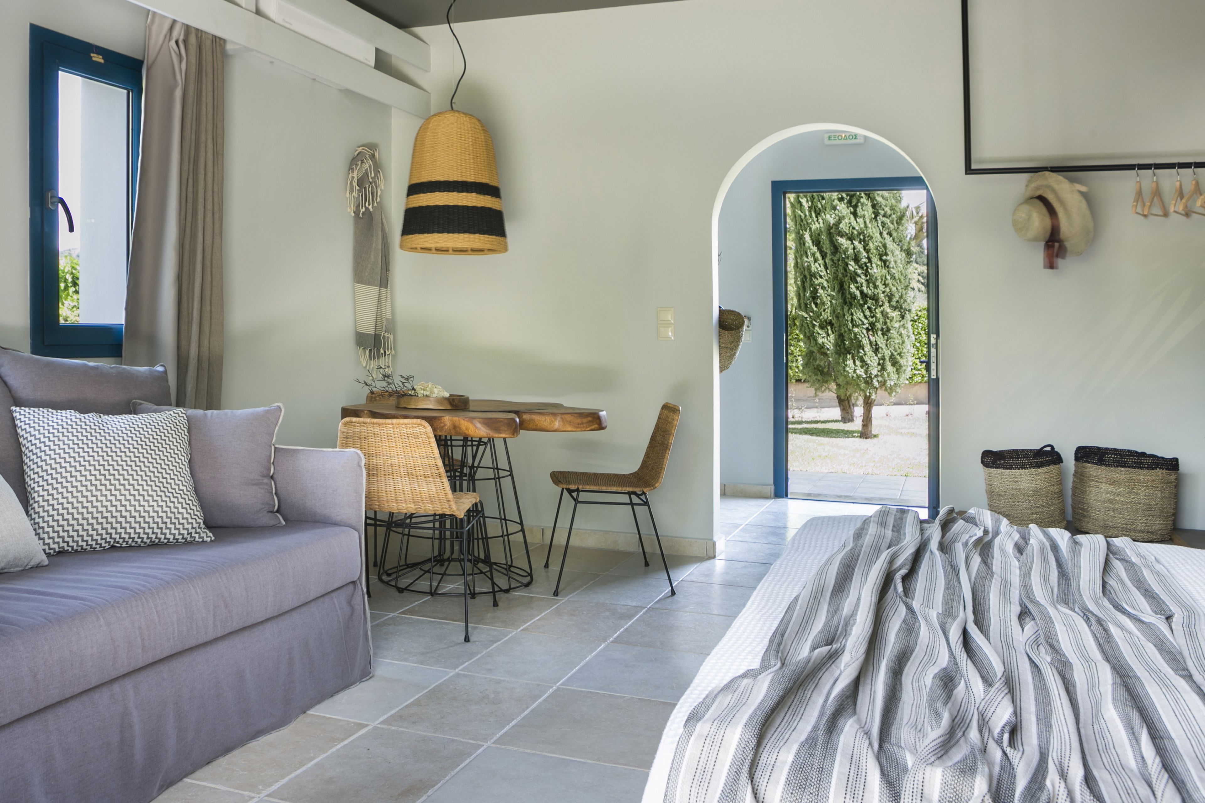 A modern bedroom with a sofa, a bed with striped bedding, a dining area with a table and chairs, and a view of the outdoors.
