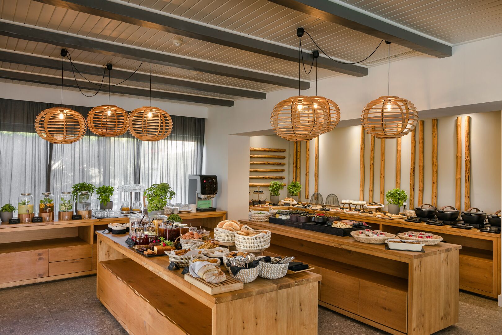 Un buffet de petit-déjeuner proposant une variété d’aliments et de boissons, des meubles en bois et des luminaires suspendus en rotin.