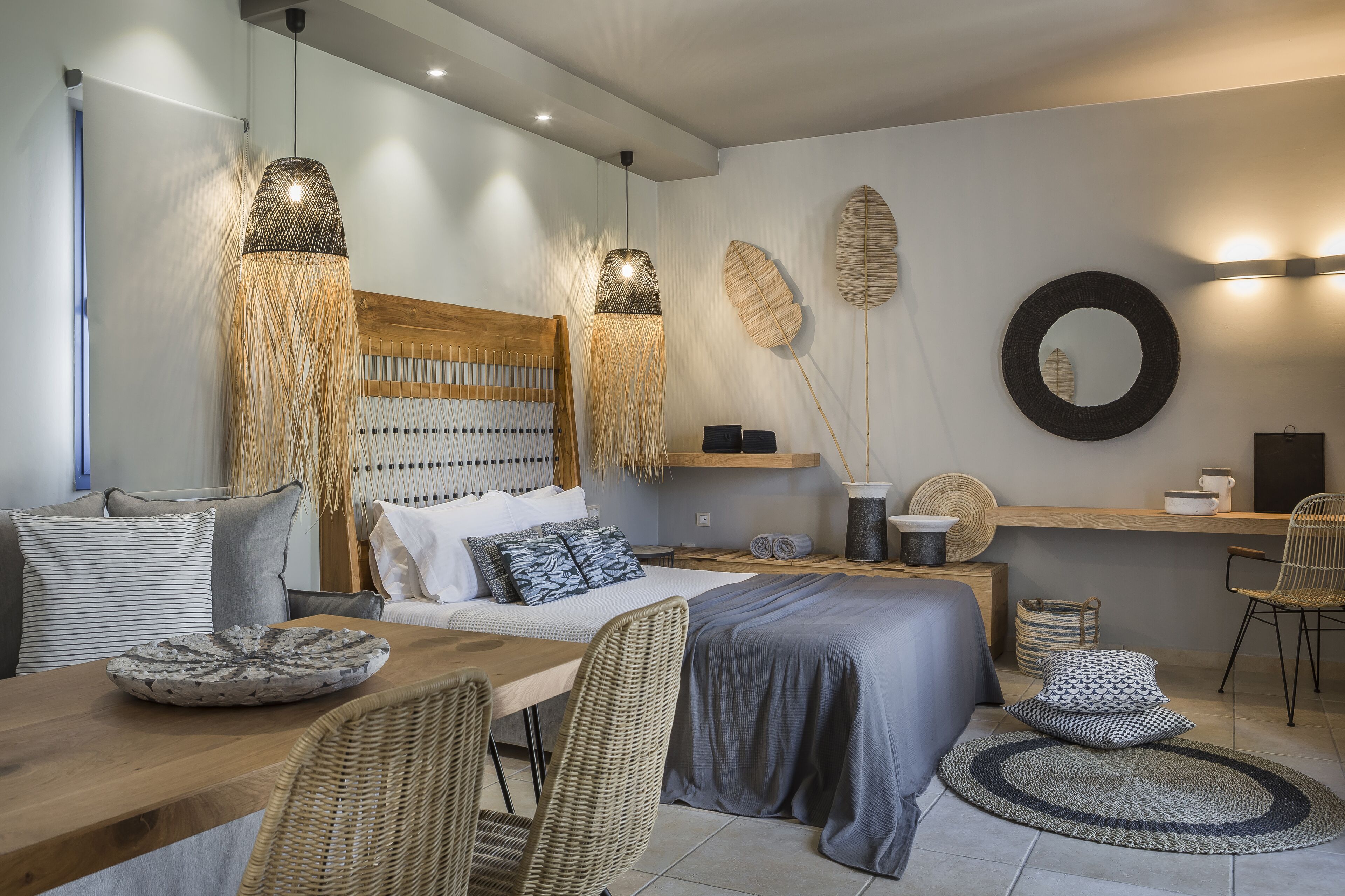 Een moderne slaapkamer met een houten hoofdbord, een groot bed, een houten eettafel, rieten stoelen en een rond tapijt.