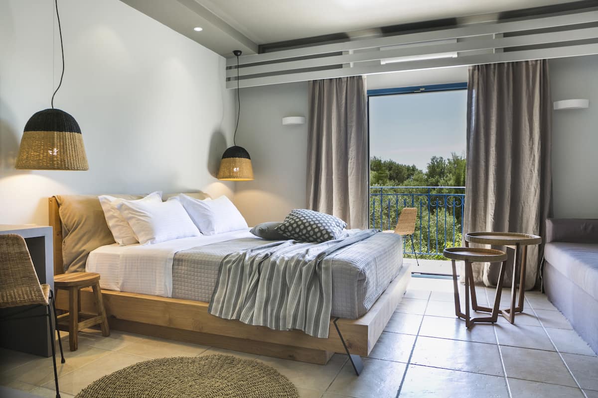 A bedroom with a bed, bedside tables, a chair, a small table, and a balcony with curtains.