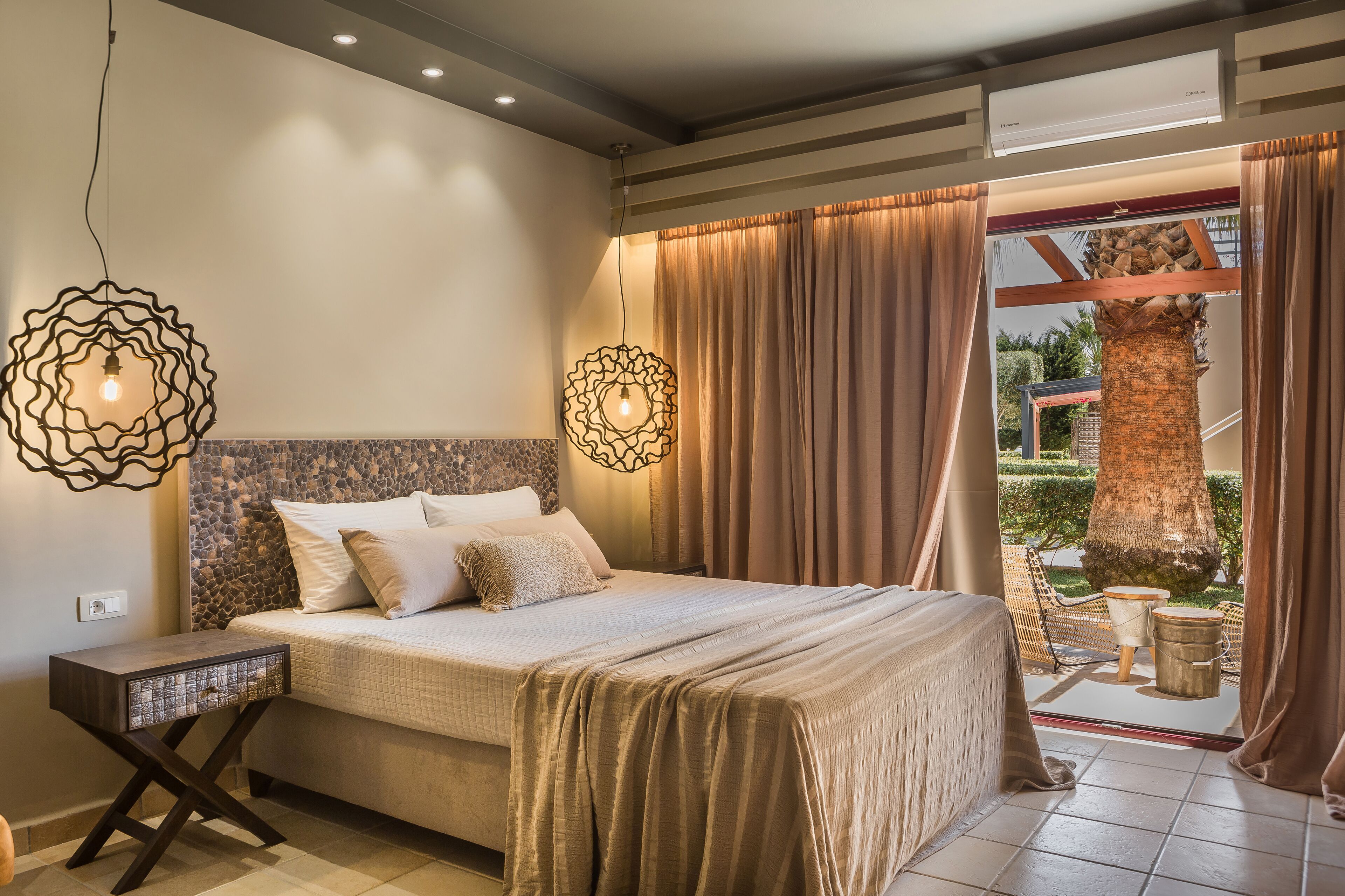 Un dormitorio con cama, mesitas de noche, lámpara colgante y vistas al exterior.