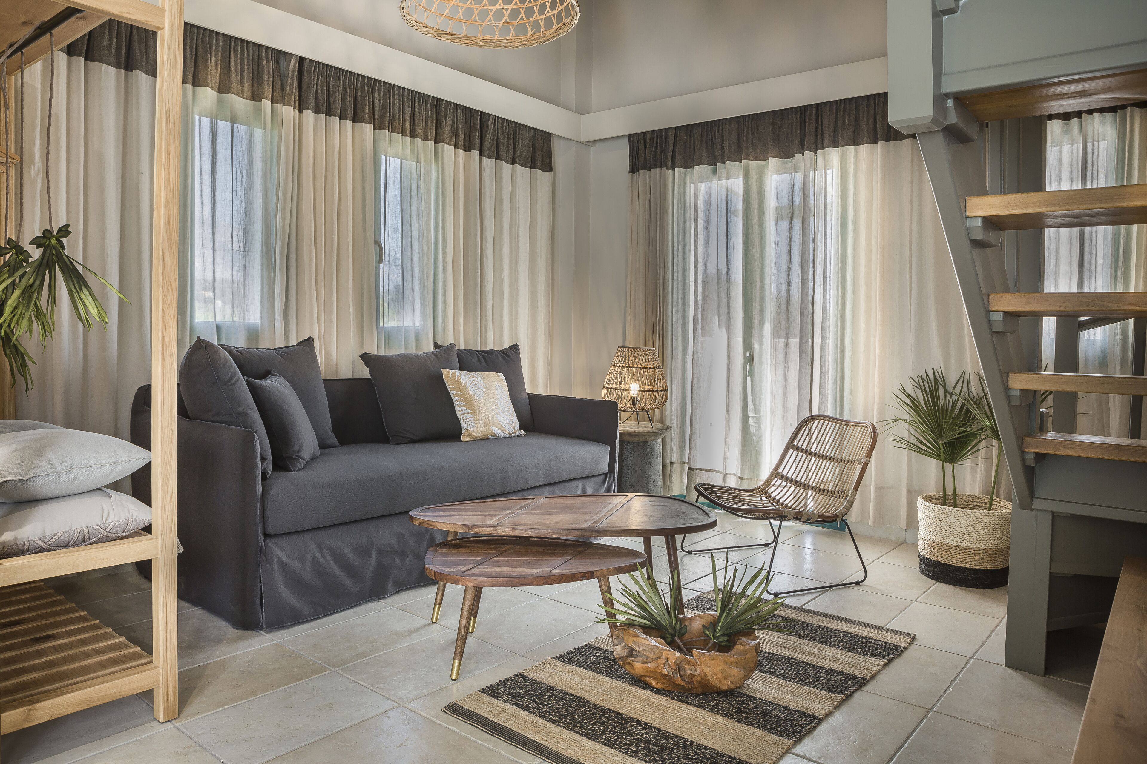Una sala de estar moderna con un sofá, una mesa de centro y una silla. Se ve una escalera a la derecha y una planta en la esquina.