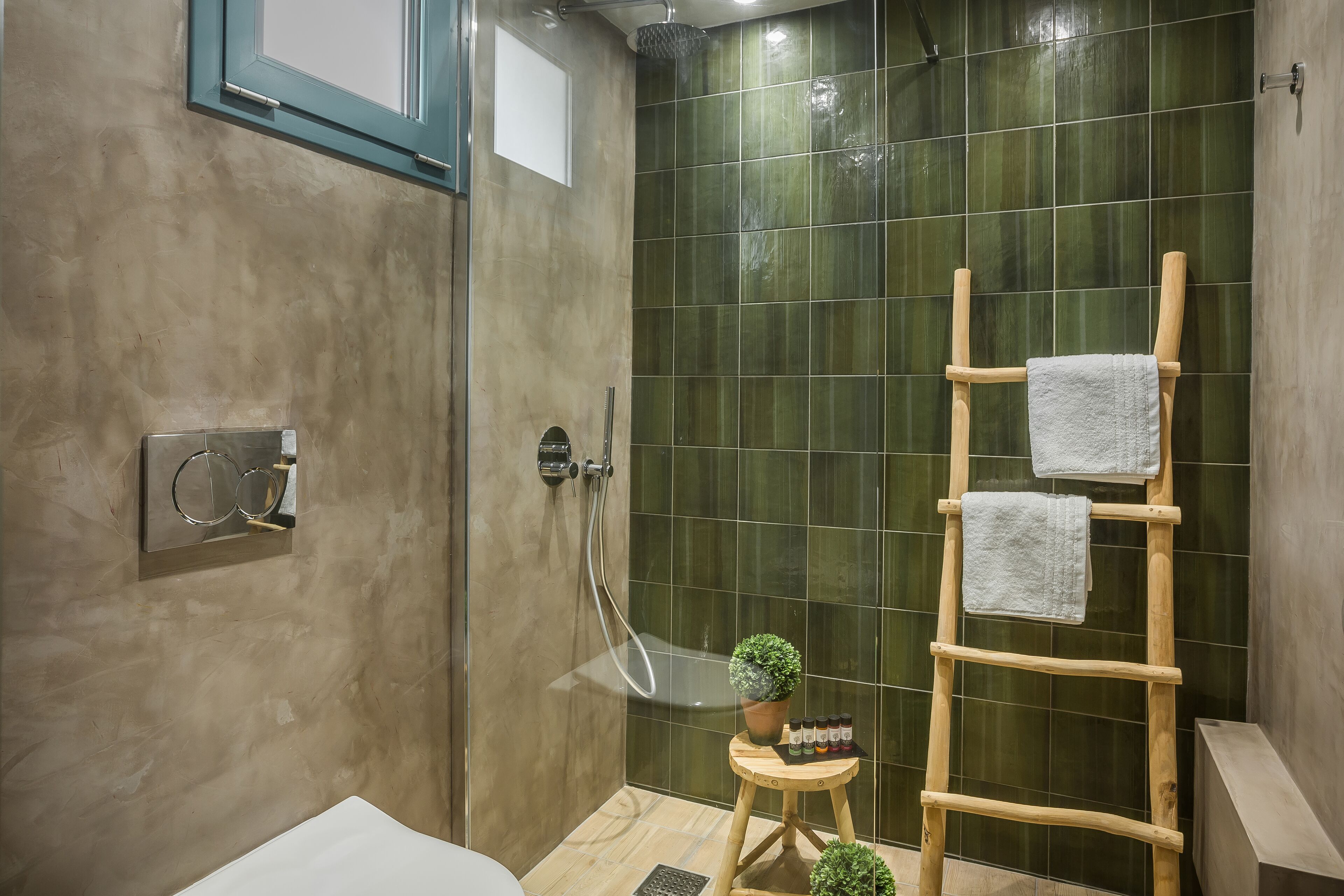 A modern bathroom with a shower, a wooden ladder with towels, a small stool with a plant, and a mirror.