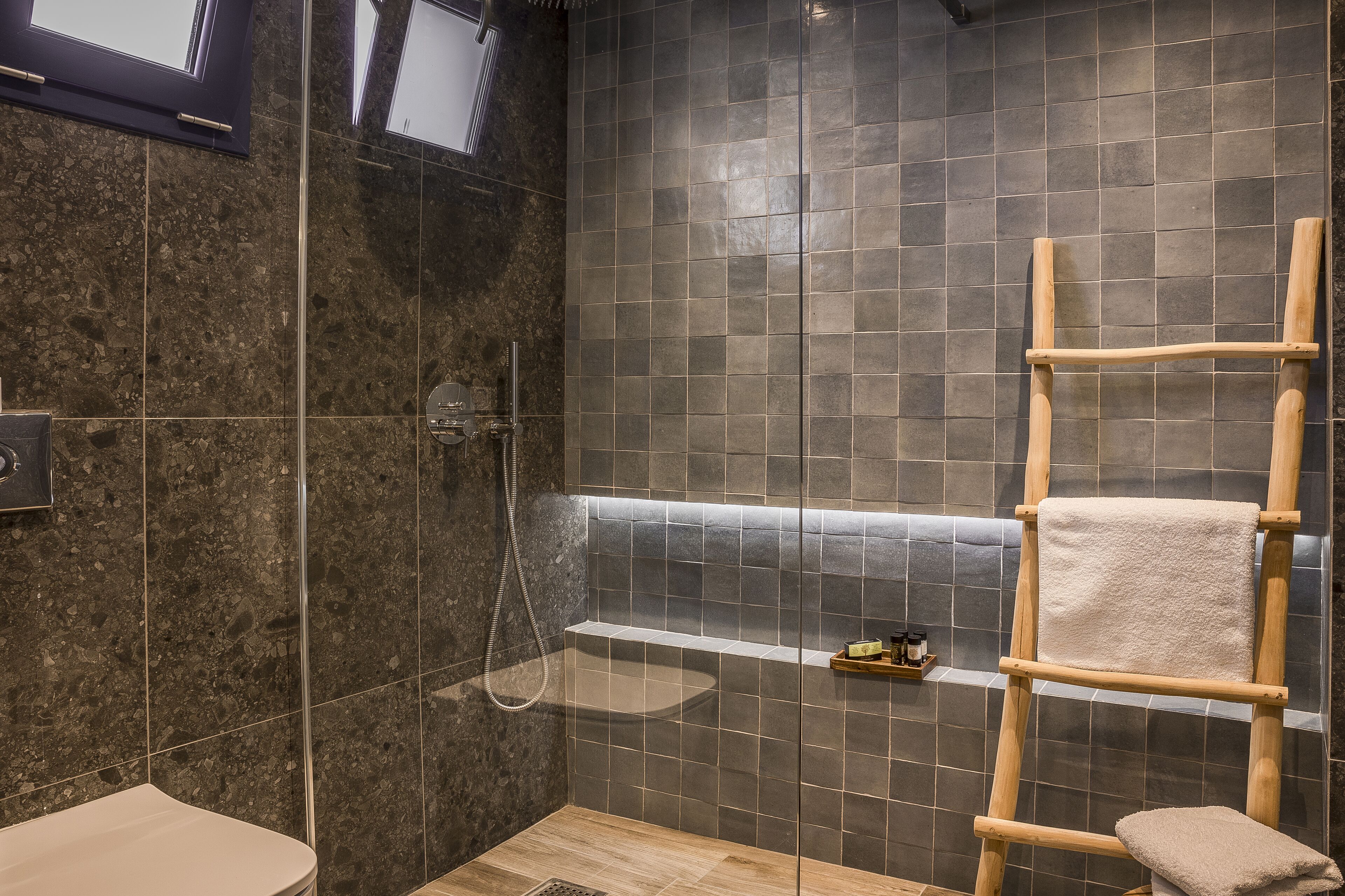 Un baño moderno con ducha, una escalera de madera y un estante con artículos de aseo.