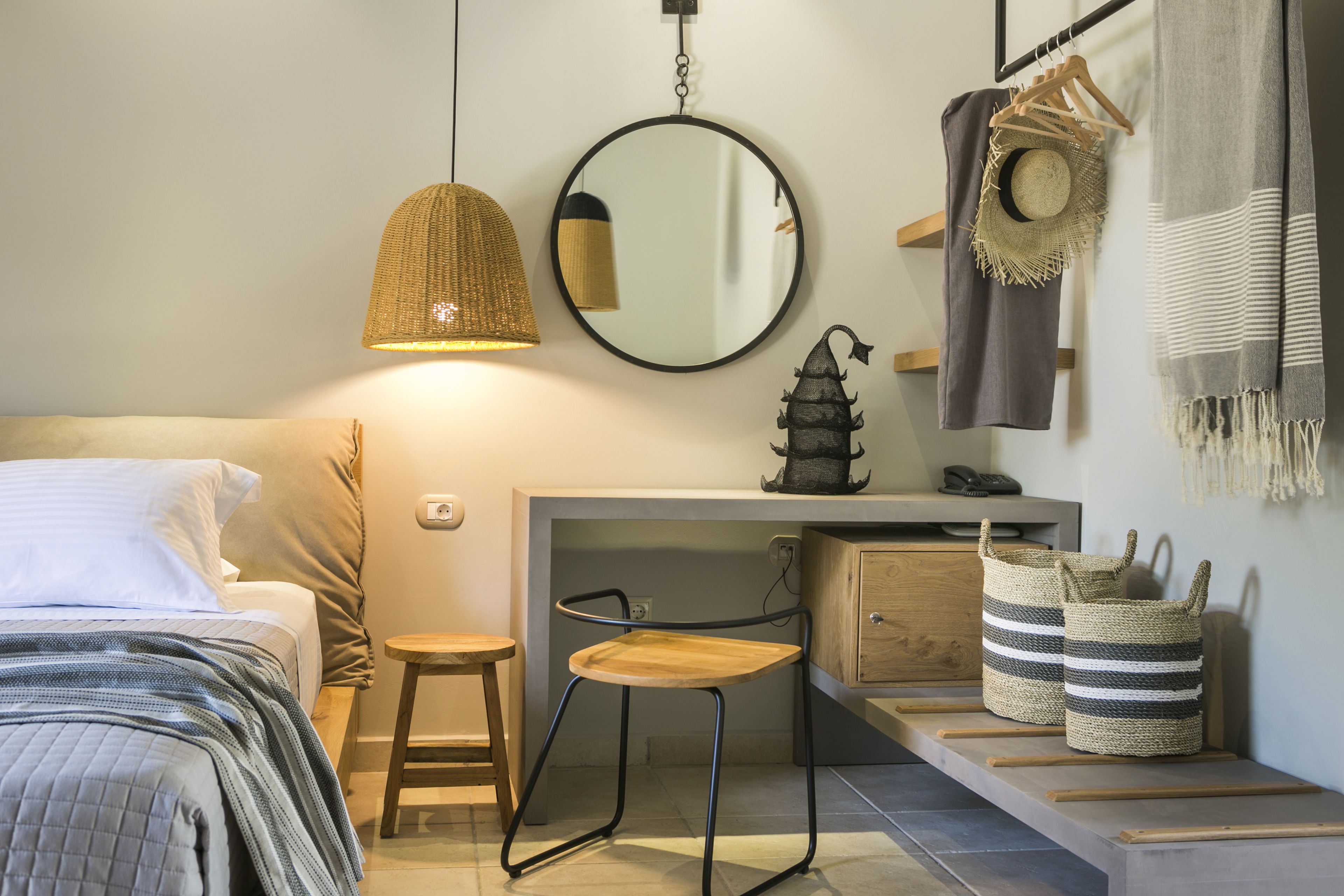 Una camera da letto con un letto, una scrivania, una sedia, una lampada a sospensione, uno specchio e una mensola a muro con oggetti decorativi.