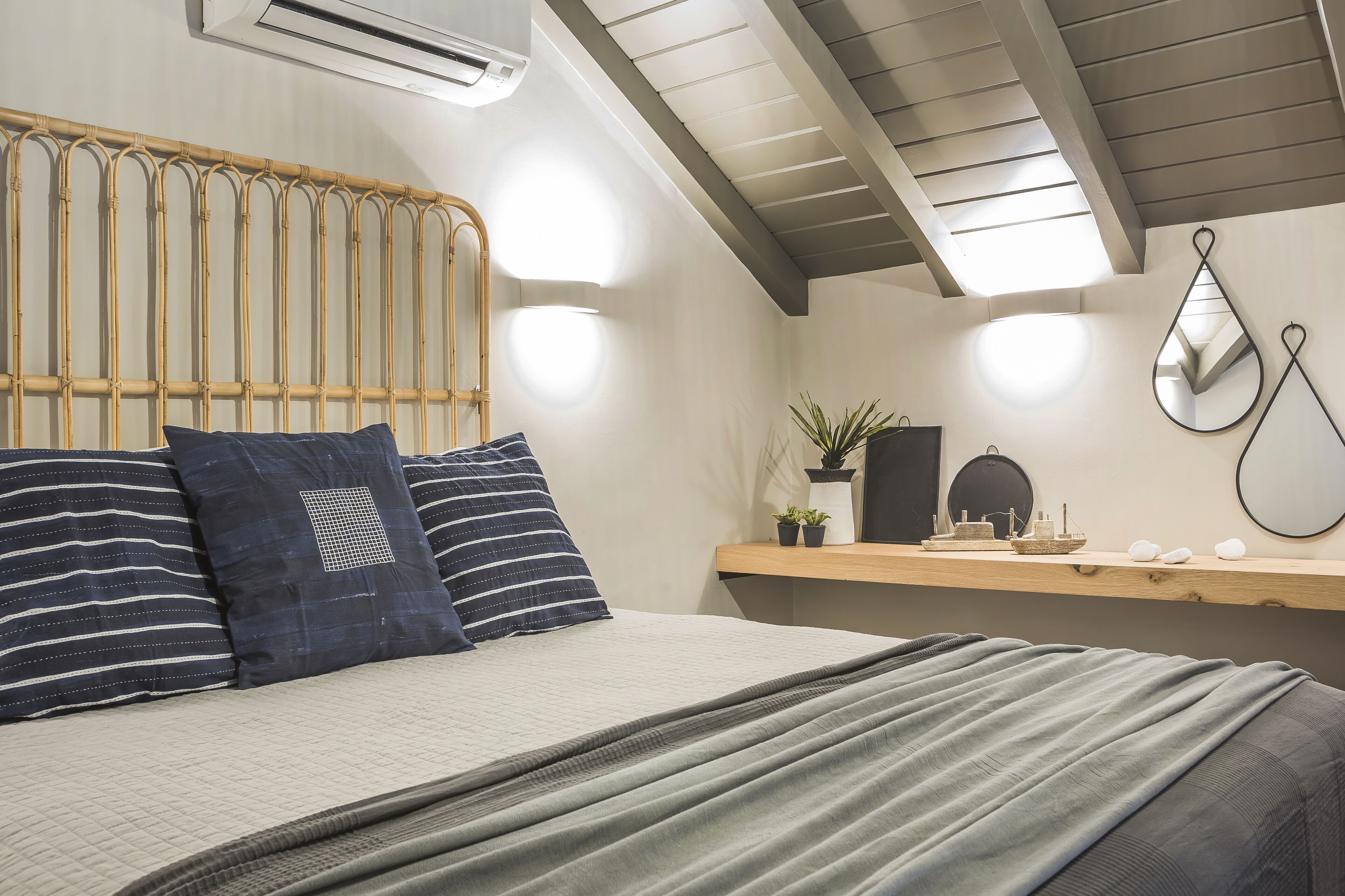 Ein Schlafzimmer mit einem Bett, einem Kopfteil, Nachttischen, einem Spiegel und einem an der Wand befestigten Regal mit Dekoration.