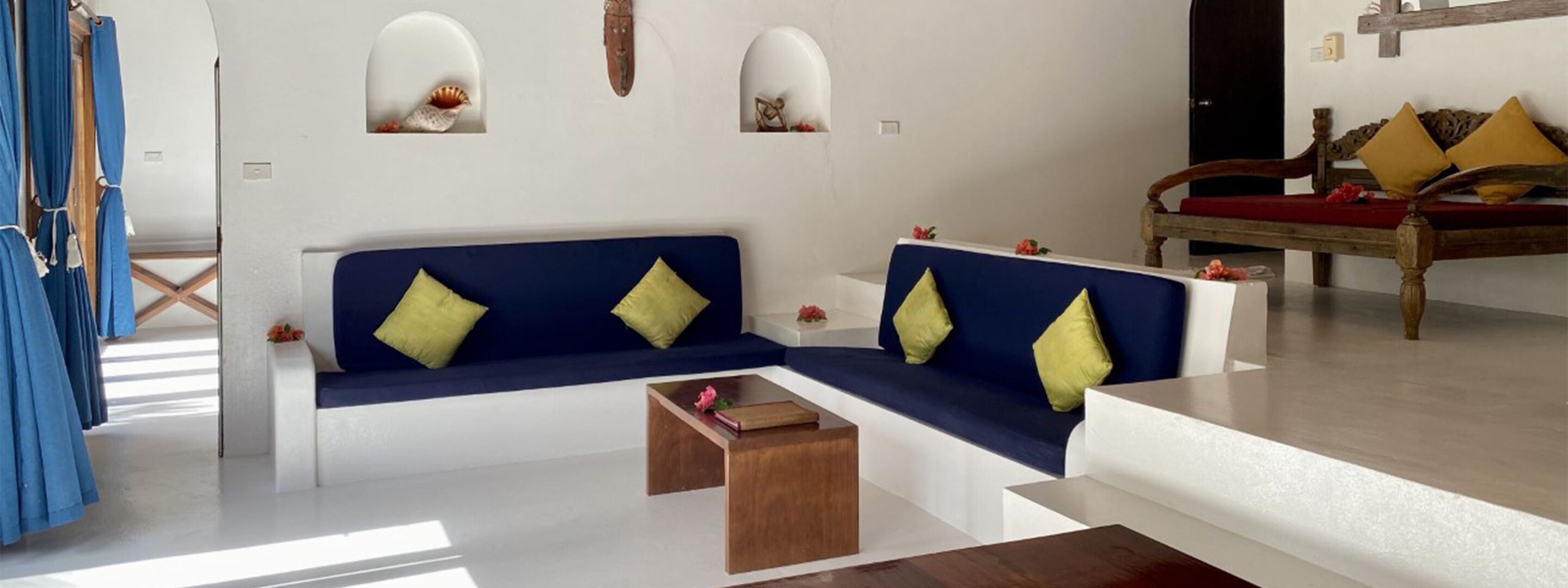 A modern living room with a blue sectional sofa, wooden coffee table, and a wooden bench with cushions.