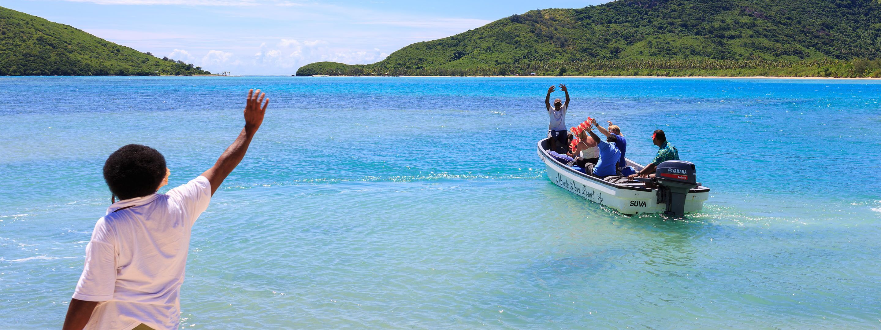 Un bote con pasajeros en un mar azul despejado, rodeado de colinas verdes y exuberantes.