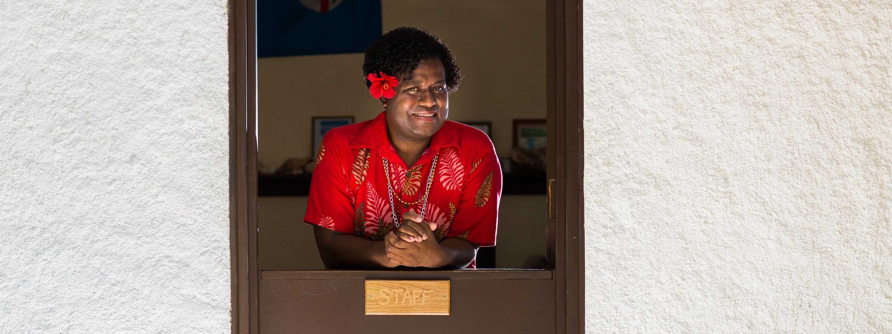 A person standing behind a counter with a "STAFF" sign, wearing a red shirt with a floral pattern.