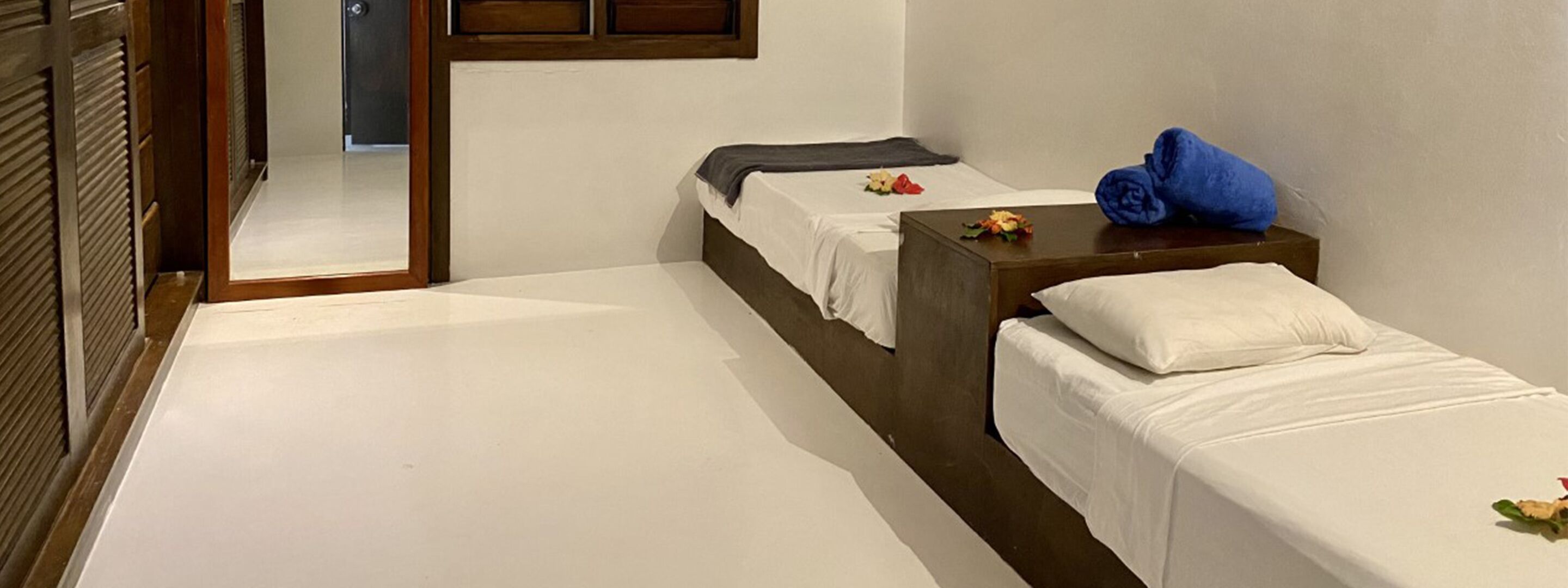 Una habitación de hotel con dos camas individuales, un cabecero de madera, una mesita con una toalla azul y un espejo en la pared.
