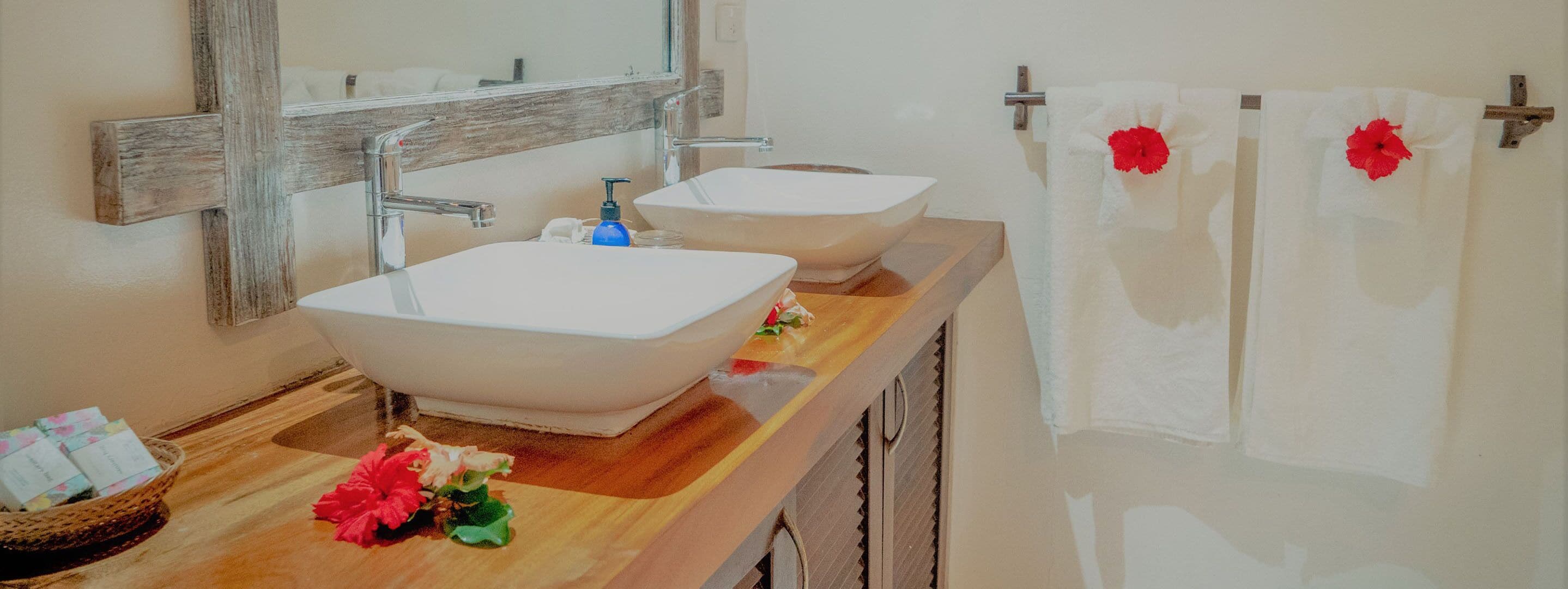 A bathroom with two large white sinks, a wooden vanity, a mirror, and two towels with red flowers.