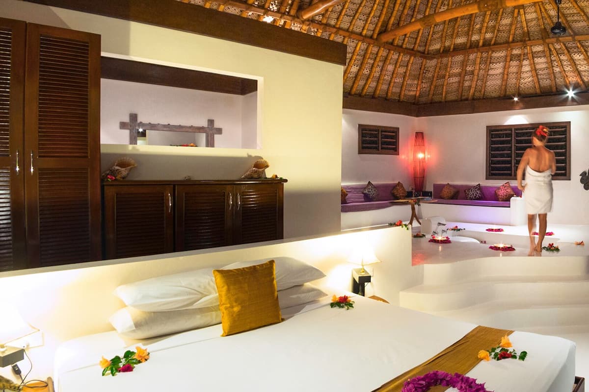 A modern hotel room with a large bed, a sofa, and a small table. There is a staircase leading to an outdoor area.