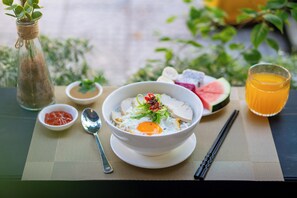 Une table dressée pour le repas, avec un bol de soupe, un verre de jus d’orange et divers condiments.