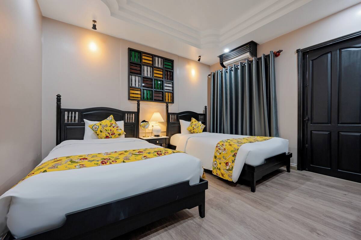A hotel room with two beds, a bookshelf, a lamp, and a large wardrobe.