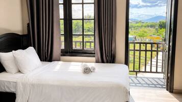 A hotel room with two beds, a large window with curtains, an air conditioning unit, and a view of greenery and buildings outside.