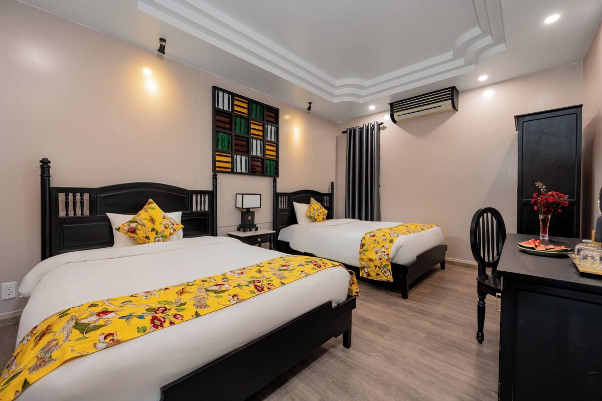 A hotel room with two beds, a desk, a chair, a bookshelf, and a decorative vase.