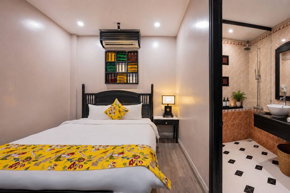 A hotel room with a bed, bedside table, lamp, and a bathroom with a sink and shower.