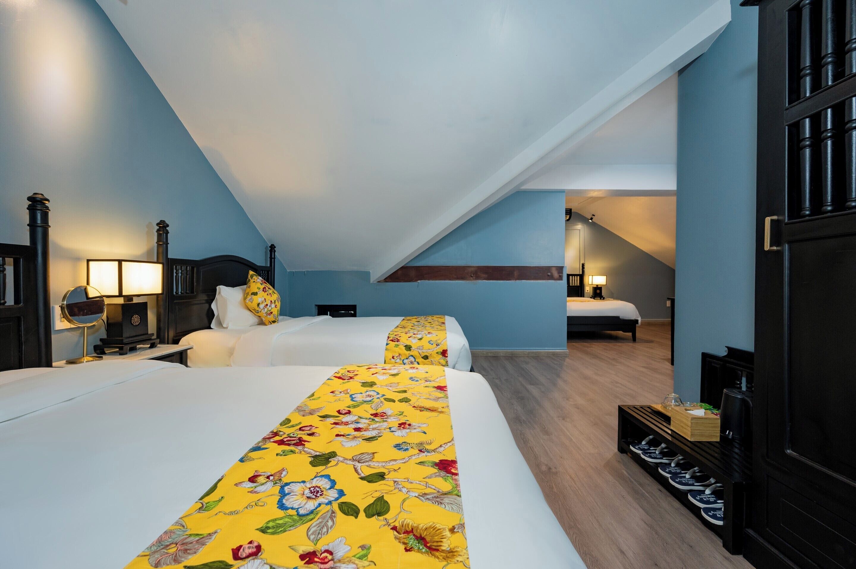 A hotel room with two beds, a wooden floor, a shoe rack, and a staircase leading to another room.