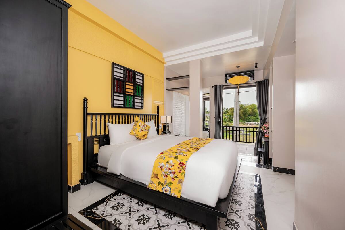 A hotel room with a bed, a yellow wall, a balcony with a view, and a window with curtains.
