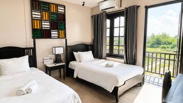 A hotel room with two beds, a desk, a window with curtains, and a view of greenery.