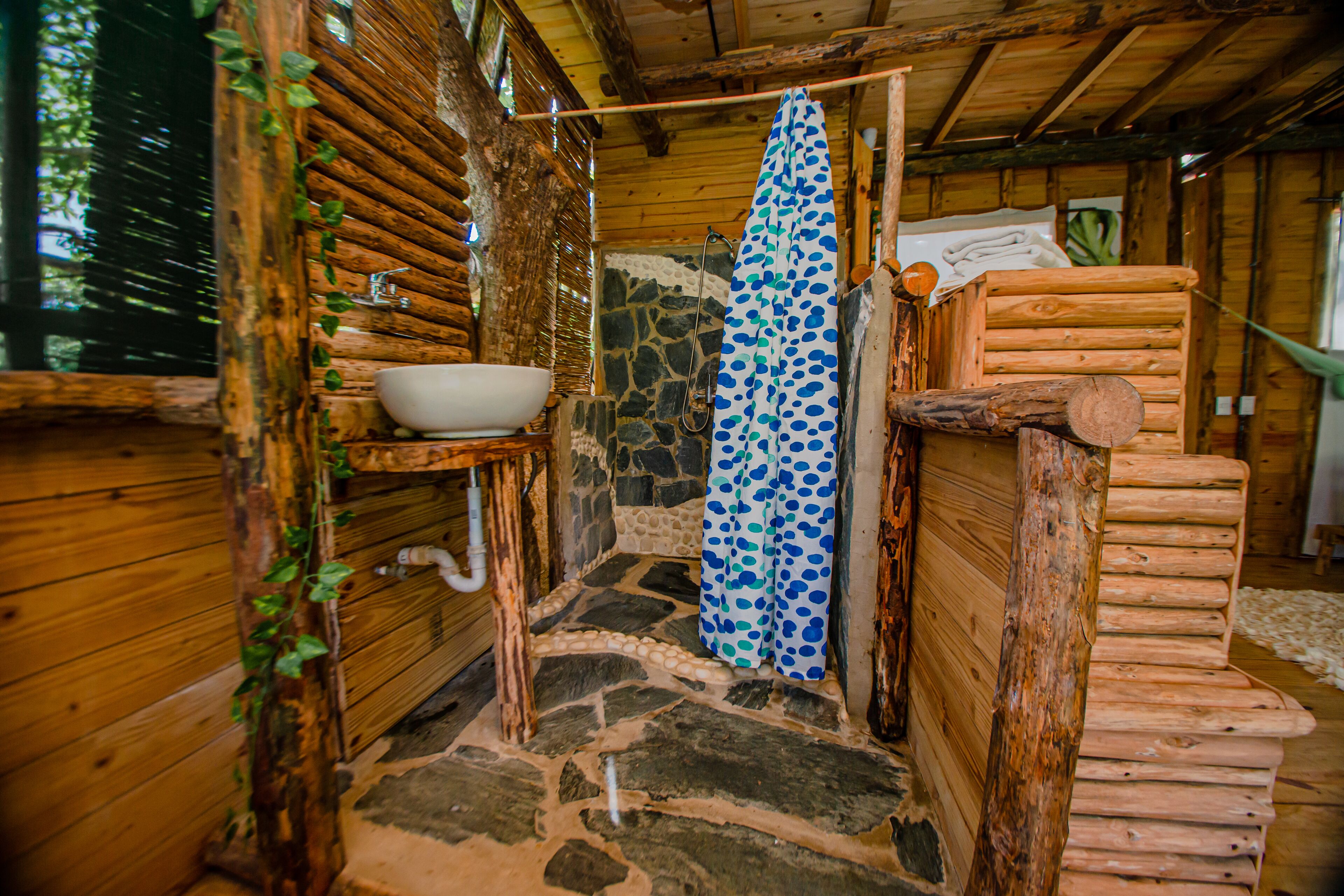 Un baño rústico de madera con suelo de piedra, un lavamanos y una cortina de ducha.