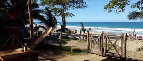Vista de la playa con una terraza de madera, una tabla de surf y una valla que da al océano.