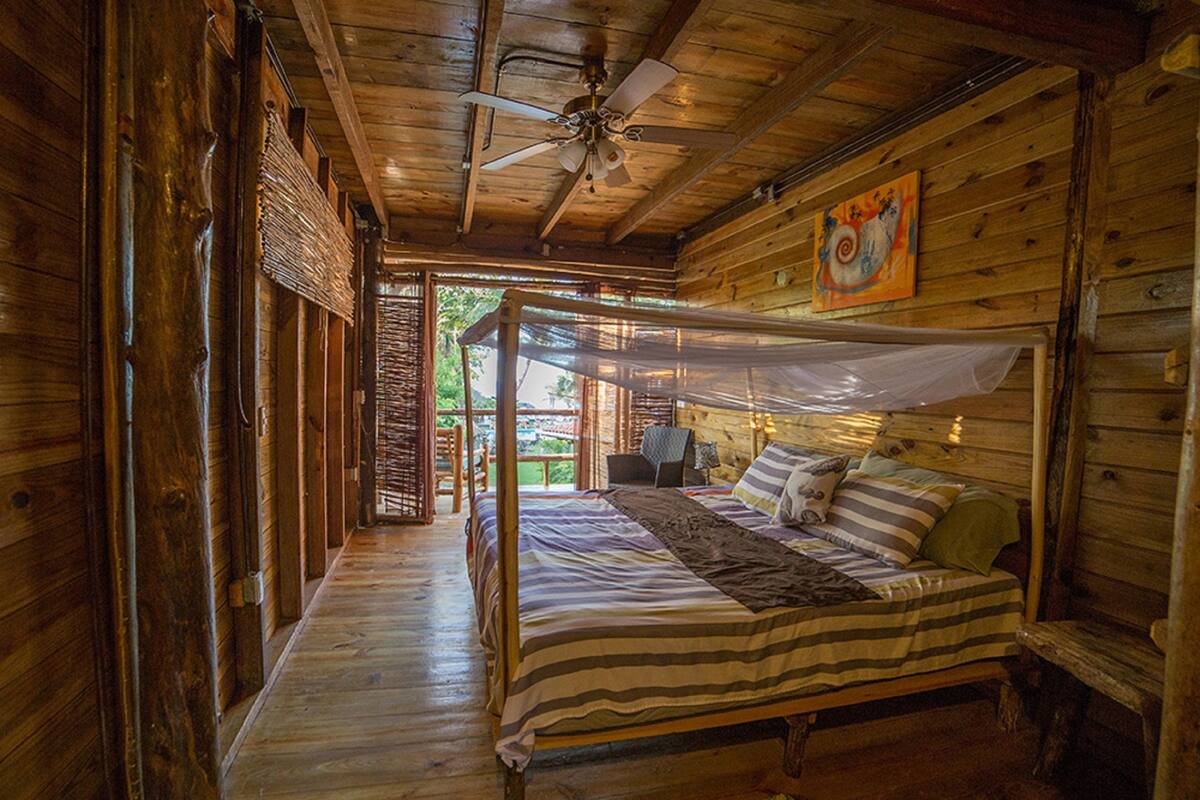 Una cabaña de madera con cama con dosel, ventilador de techo y un cuadro en la pared.