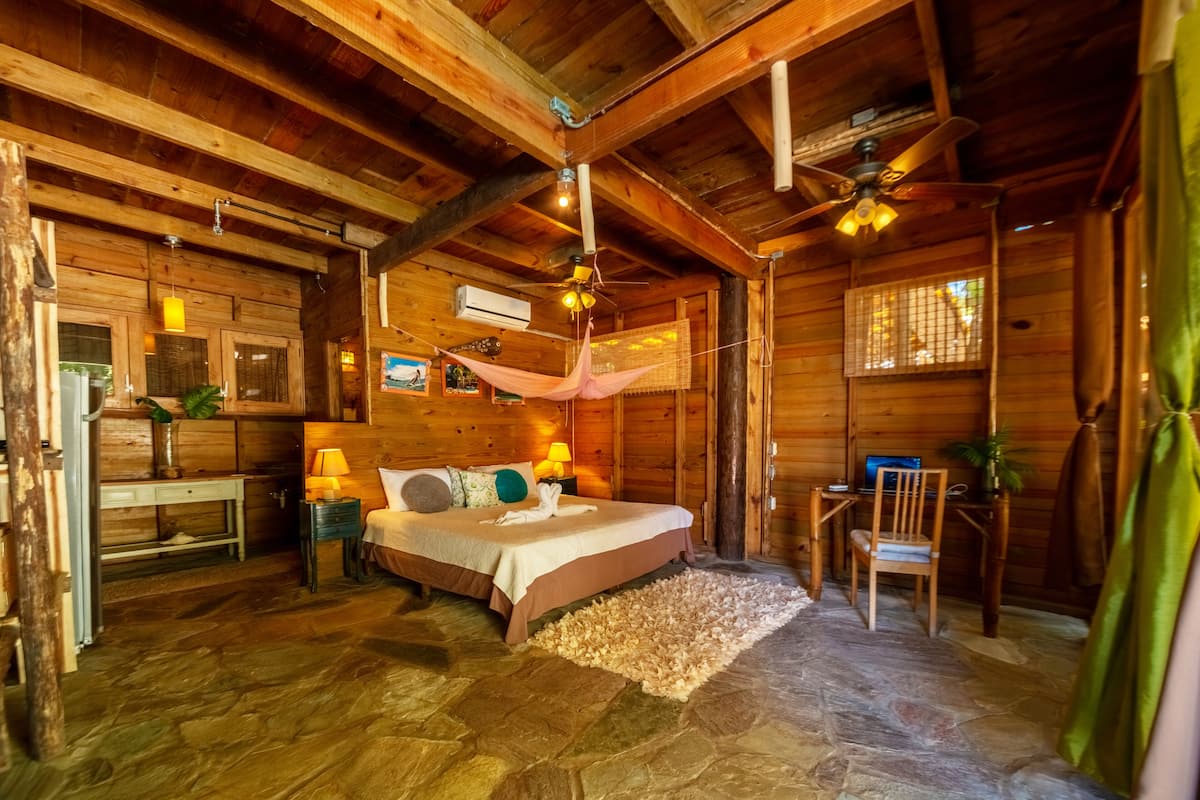 Un dormitorio rústico de cabaña de madera con una cama, mesitas de noche, un escritorio y una silla.