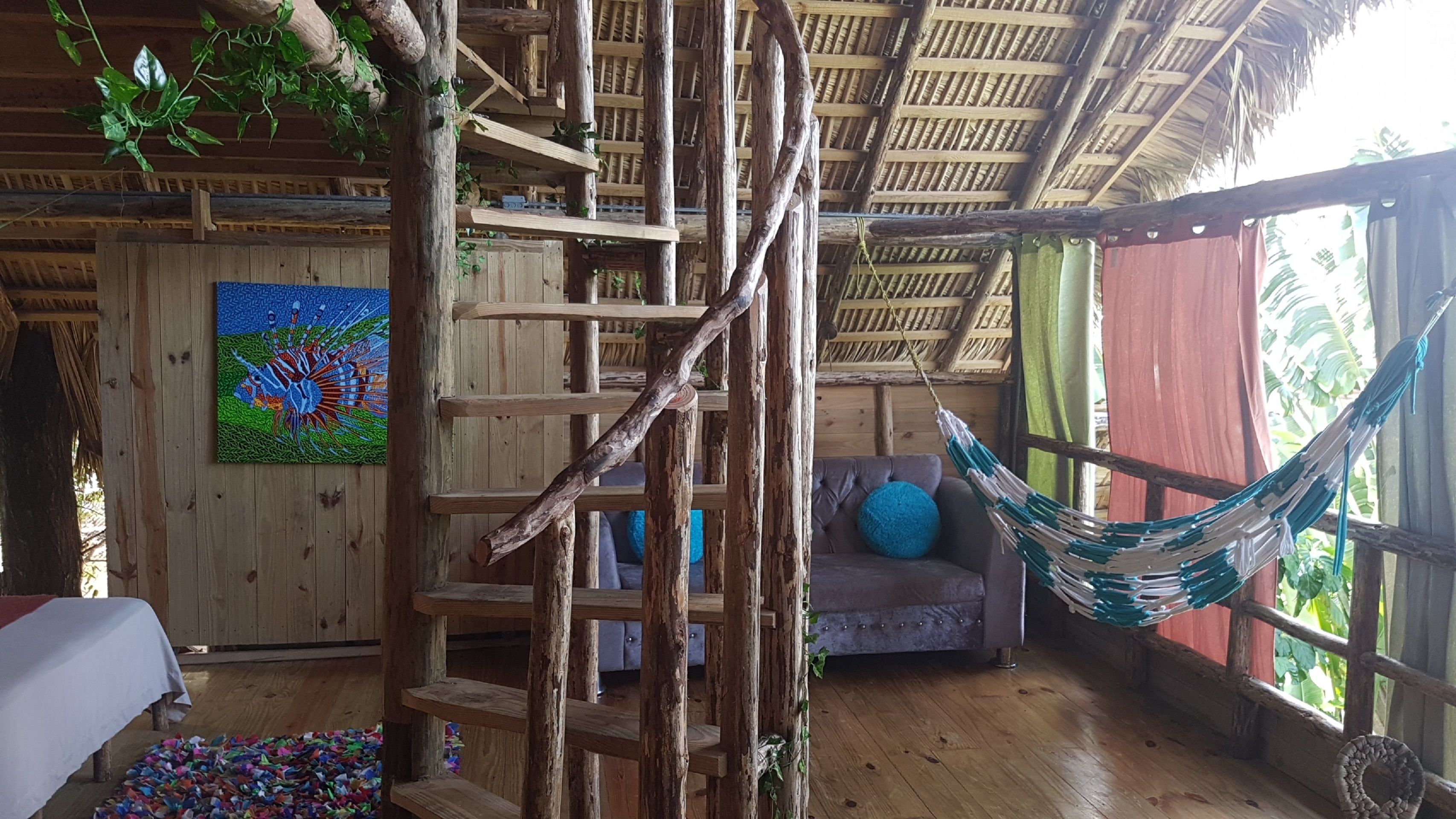 A rustic wooden room with a hammock, a sofa, and a colorful painting on the wall.