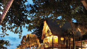 A wooden house with a thatched roof, a stone pathway, and a pool area.