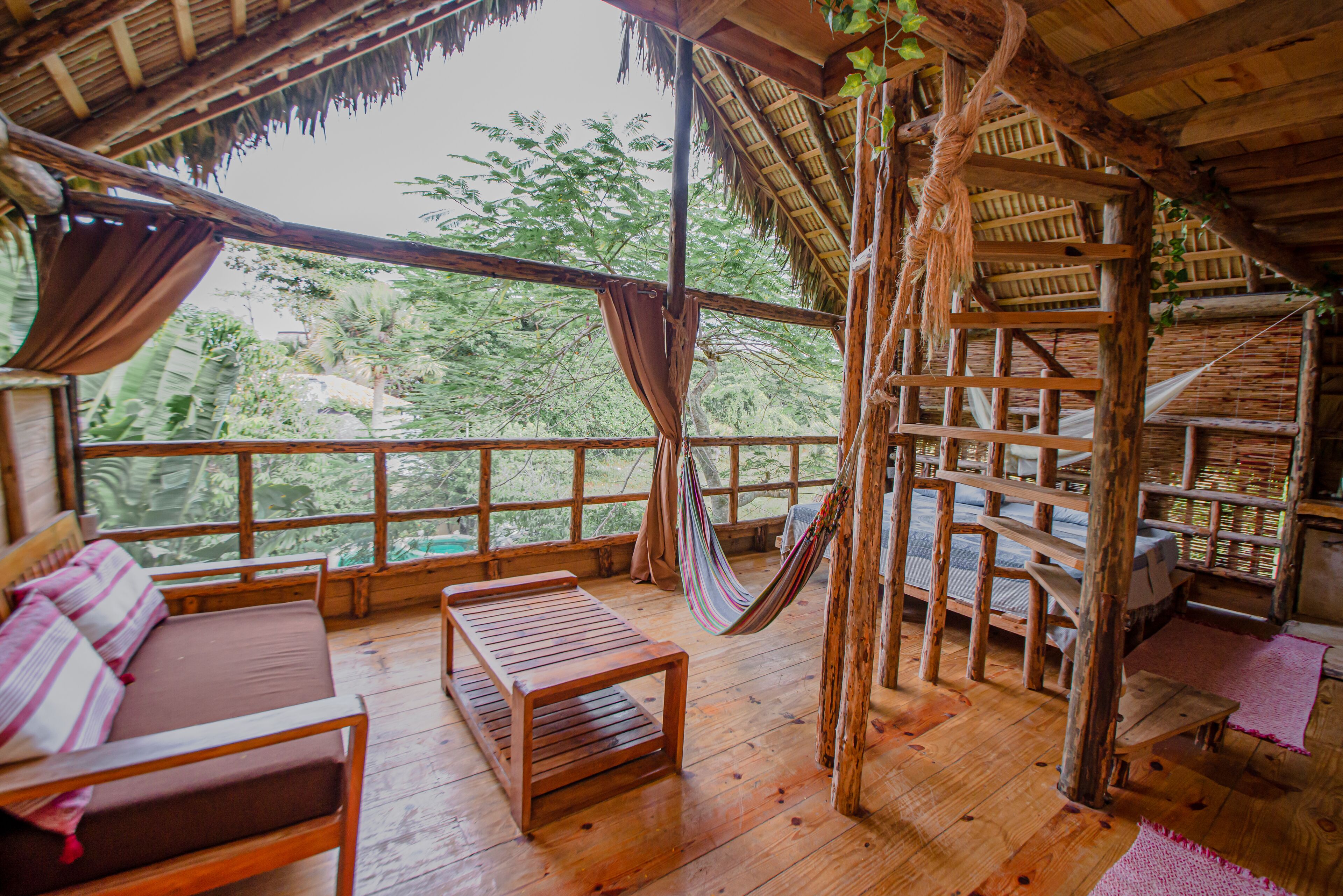 A wooden room with a hammock, wooden furniture, and a view of the outdoors.