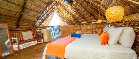 A room with a high wooden ceiling, a bed with white and orange bedding, and a woven hanging light fixture.