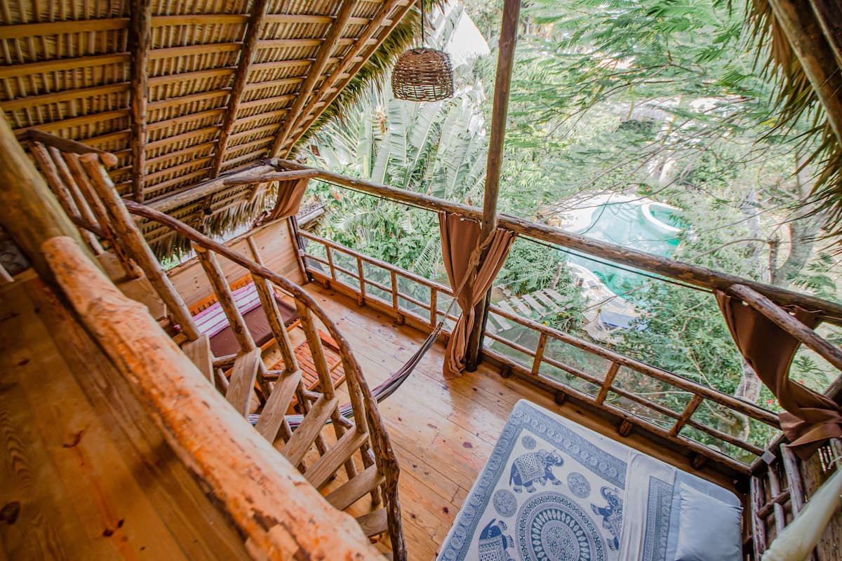 Una escalera de madera lleva a un balcón con vistas a un follaje exuberante.