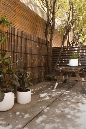 Una valla de madera, un patio de concreto y un banco de madera con una planta en maceta.