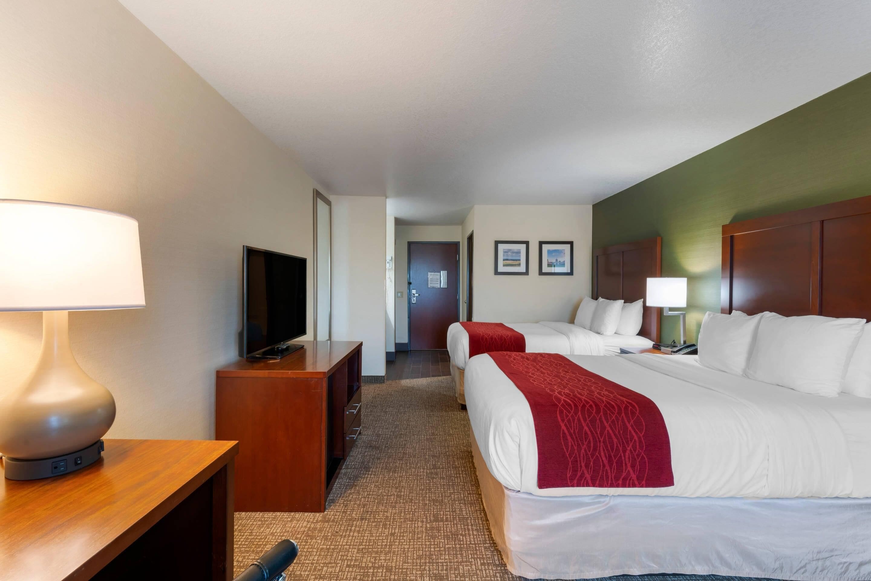 A hotel room with two beds, a TV, a desk, and a lamp.