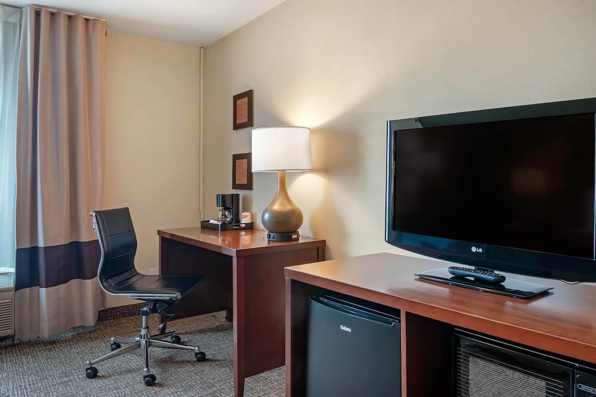 Habitación de hotel con escritorio, silla, televisor, lámpara y un refrigerador pequeño.