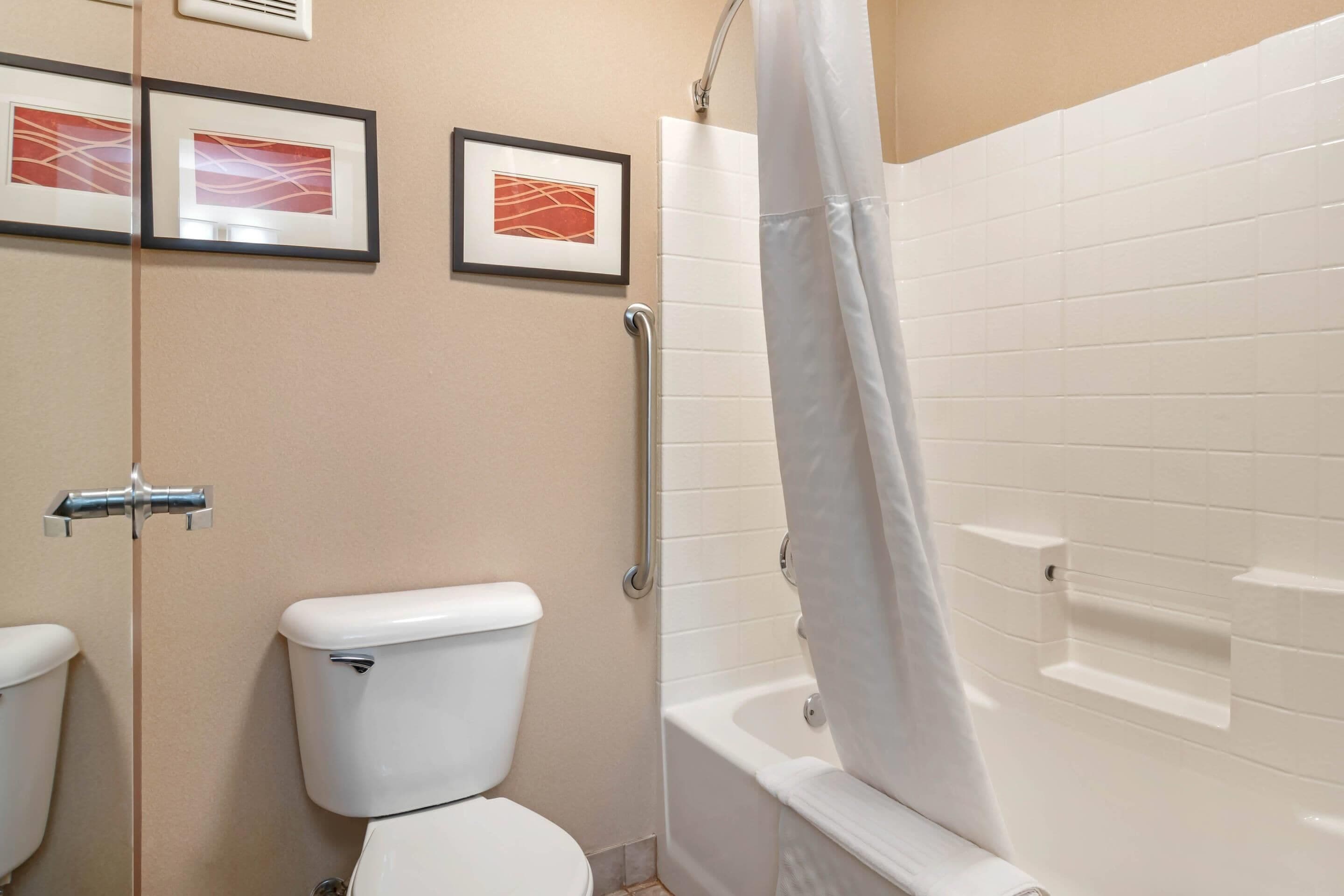 A bathroom with a toilet, a shower with a curtain, and two framed pictures on the wall.