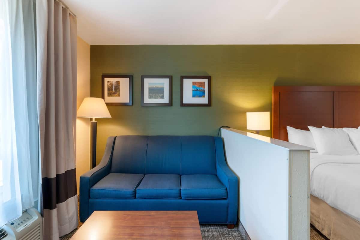 Habitación de hotel con sofá azul, cama, escritorio y tres cuadros en la pared.