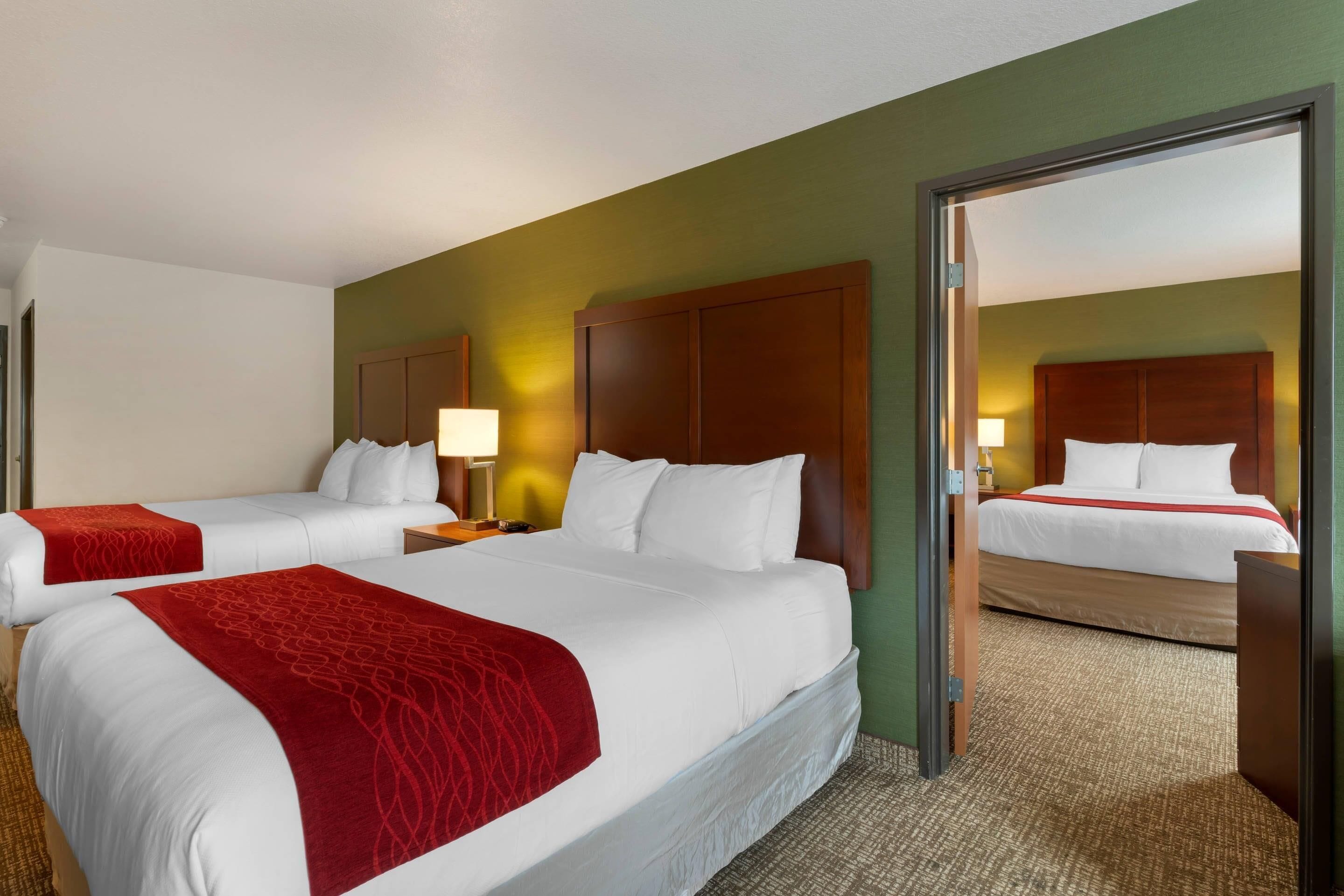 A hotel room with two beds, a wooden headboard, a red throw blanket, and a mirror reflecting the room.