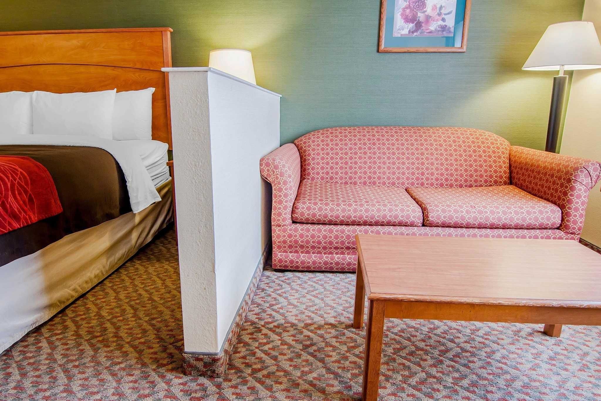 A hotel room with a bed, a sofa, a table, and a patterned carpet.