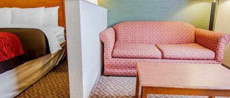 A hotel room with a bed, a sofa, a table, and a patterned carpet.