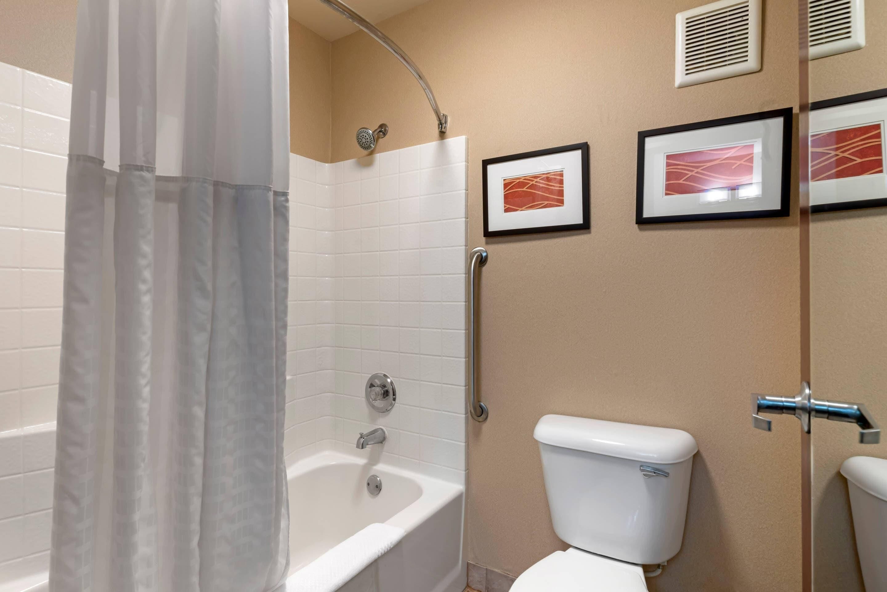 Een badkamer met een bad, toilet en een lijst met een kunstwerk aan de muur.