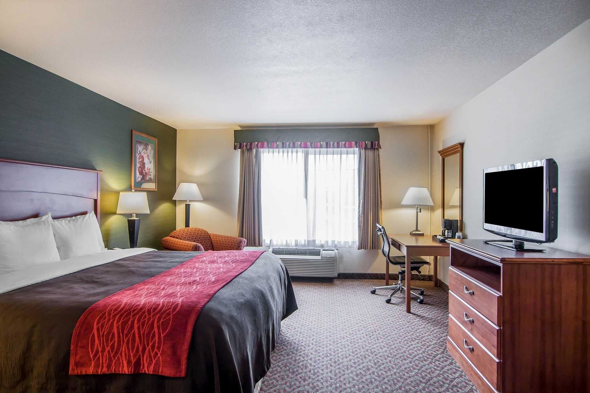 A hotel room with a bed, desk, chair, television, and a large window with curtains.