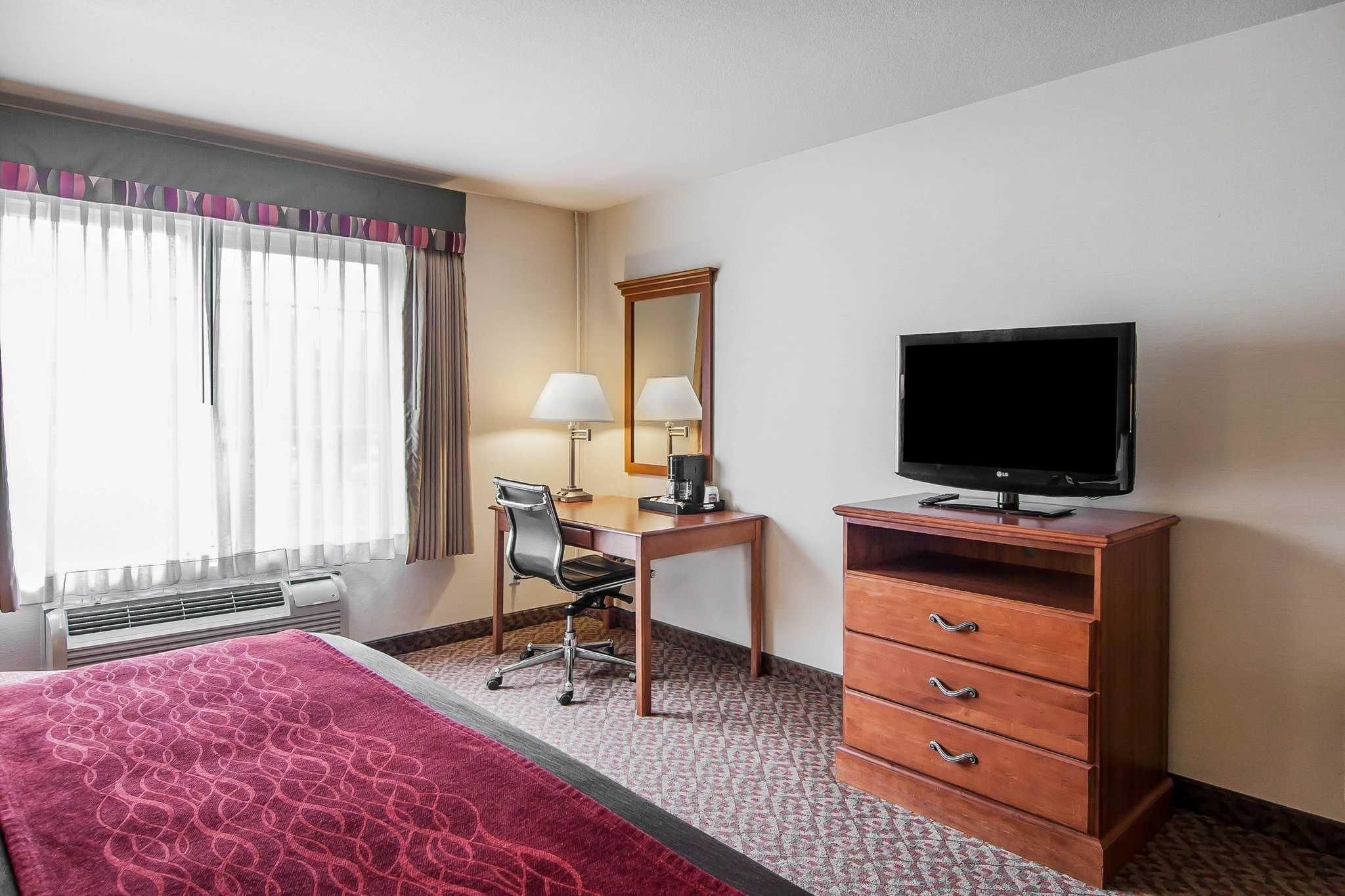Een hotelkamer met een bed, een bureau met stoel, een televisie, een kast en een raam met gordijnen.