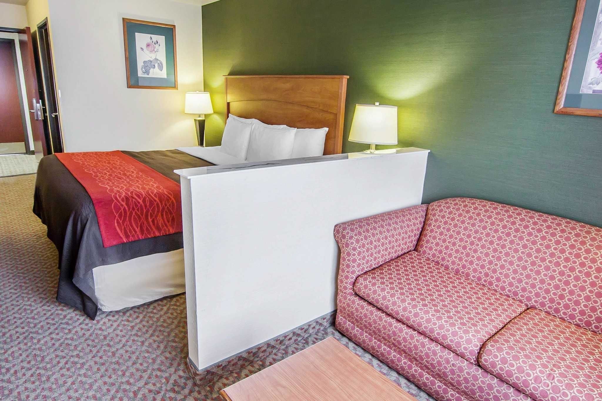 A hotel room with a bed, two bedside lamps, a red patterned sofa, and a wooden nightstand.